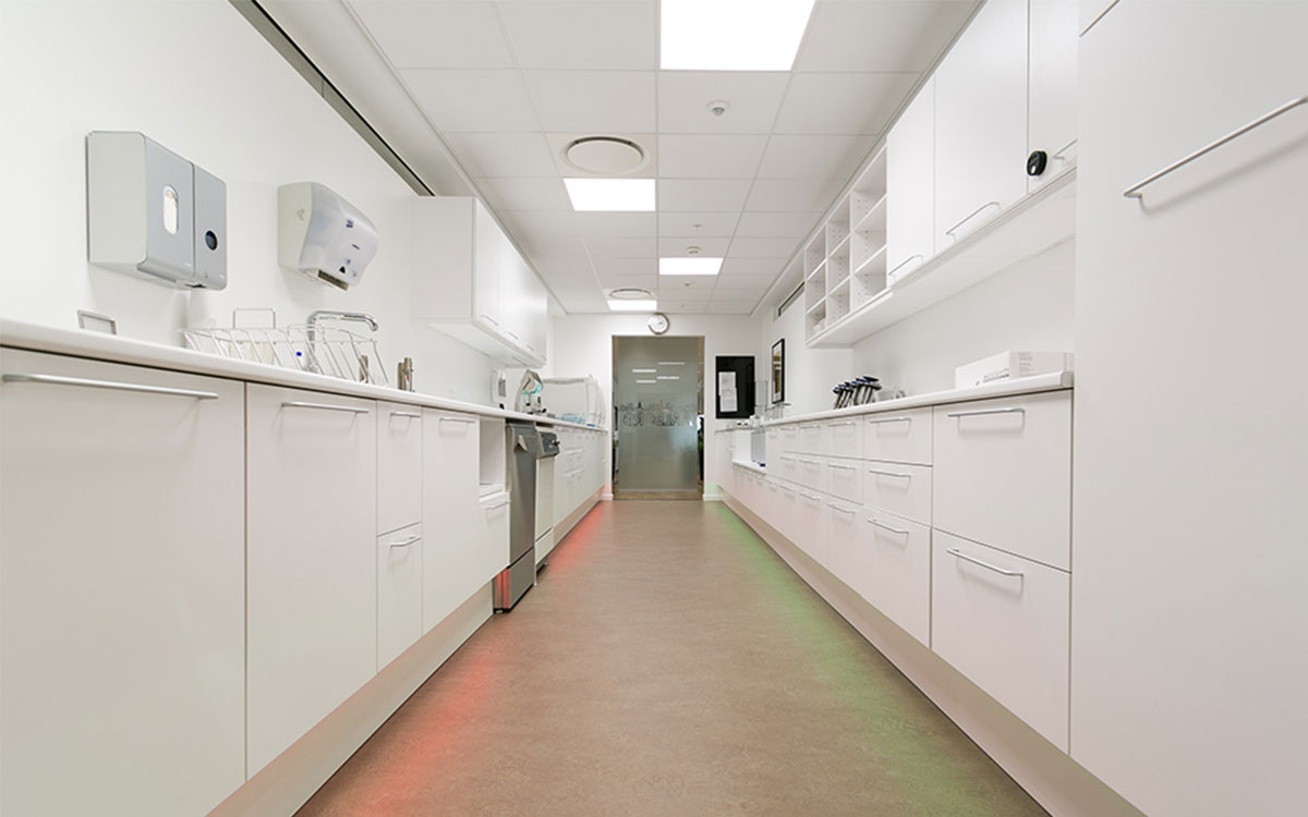 Białe pomieszczenie do sterylizacji w klinice stomatologicznej w Allborgu. Z przodu widać biała zabudowę meblową. 